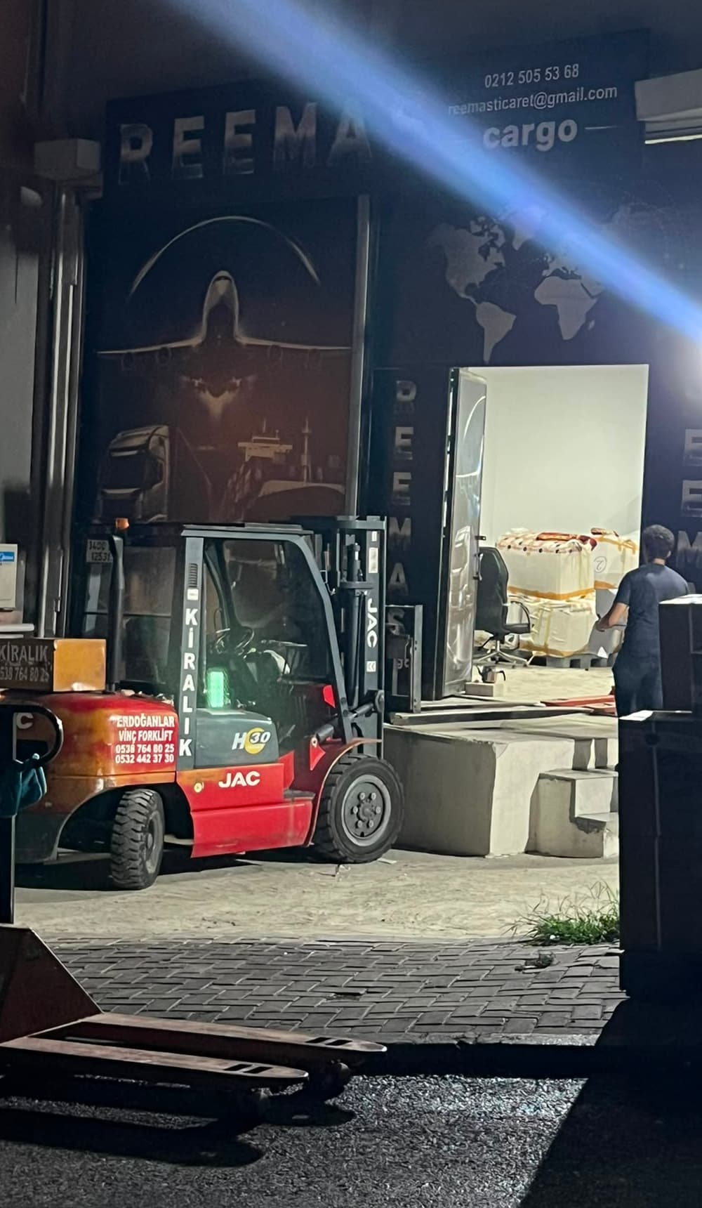 مستودع ريماس في مرتر ليلاً، ورافعة شوكية أمام الباب